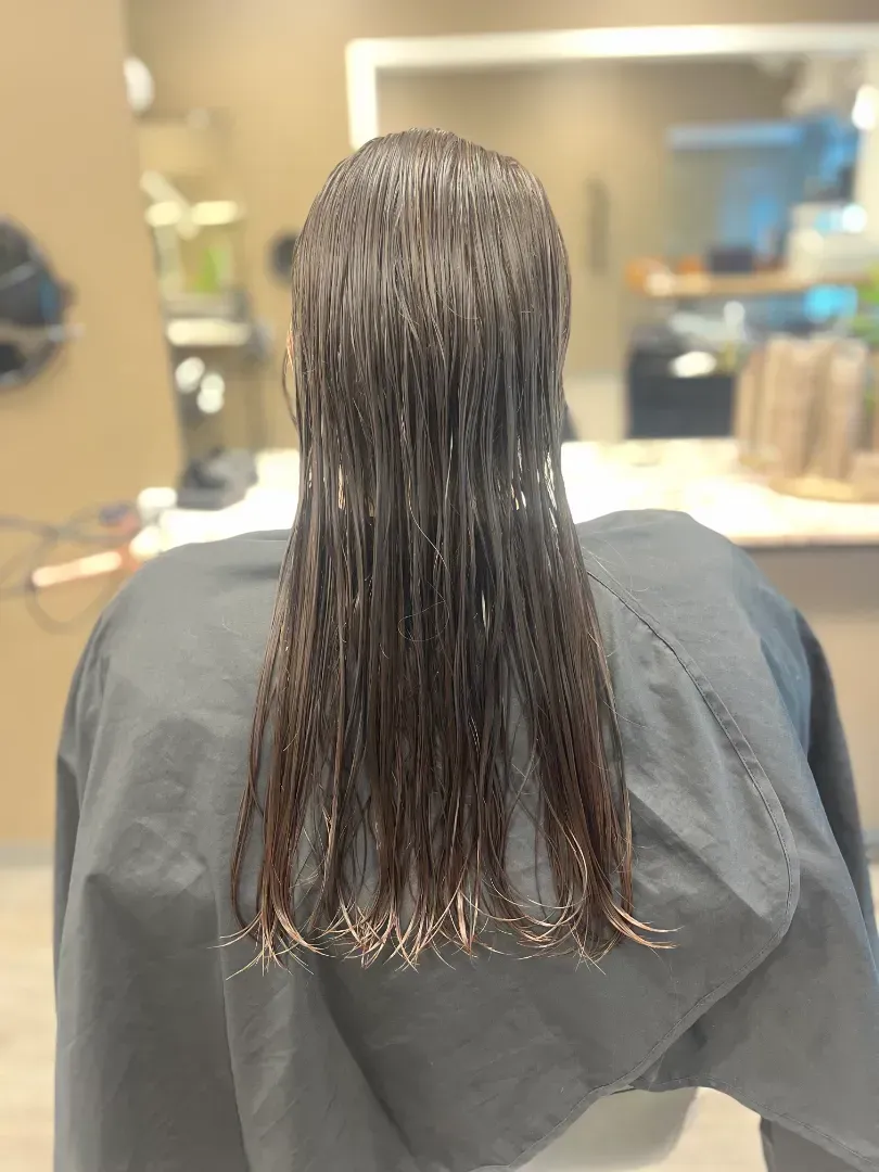 A person with wet brown hair, wearing a black cape, in a salon.