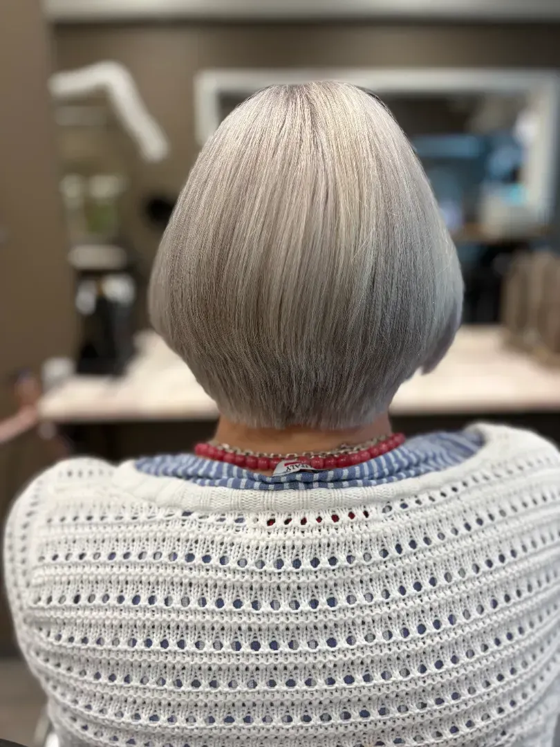 Woman with short, silver hair wearing a white sweater, back view.