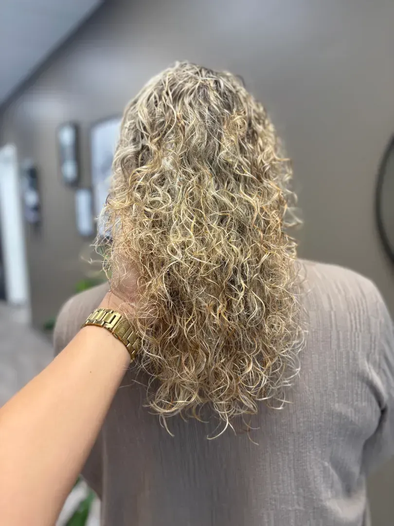 Blonde curly hair. Someone's back is facing the camera as a hand holds their hair.