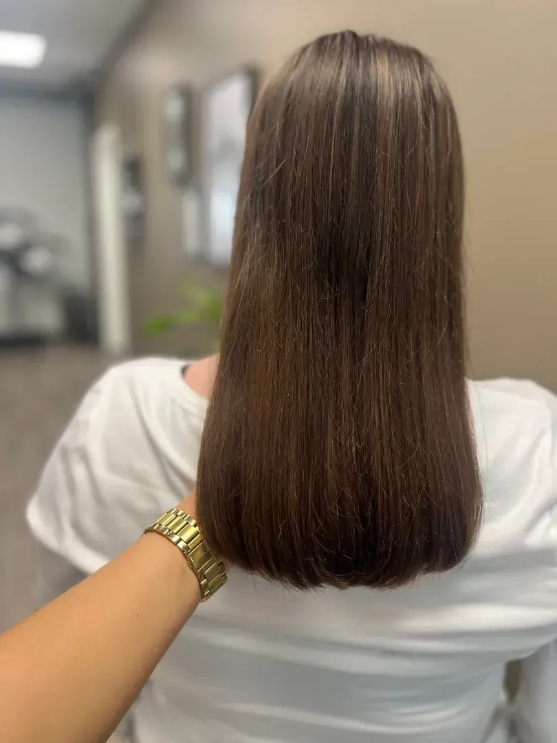 Person's straight, dark brown hair after a haircut; hand on shoulder, gold watch, white shirt in salon.