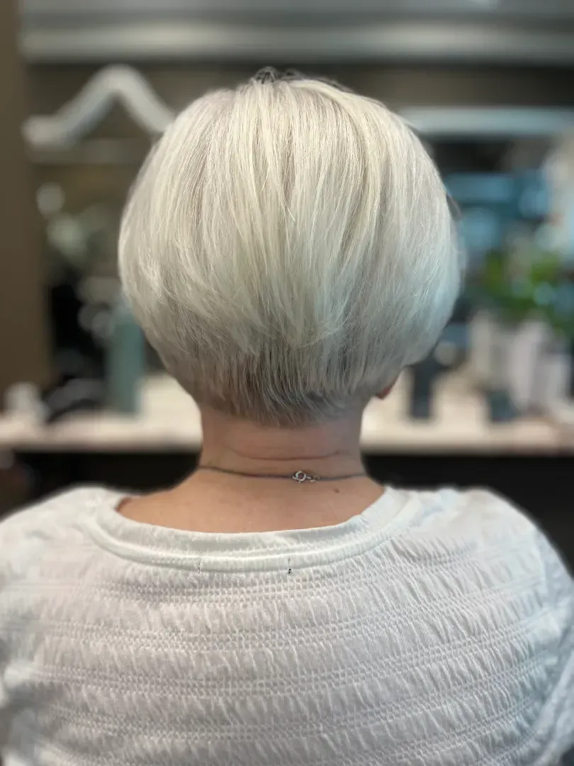 Woman with short, white, rounded haircut, seen from the back. She's wearing a white sweater.