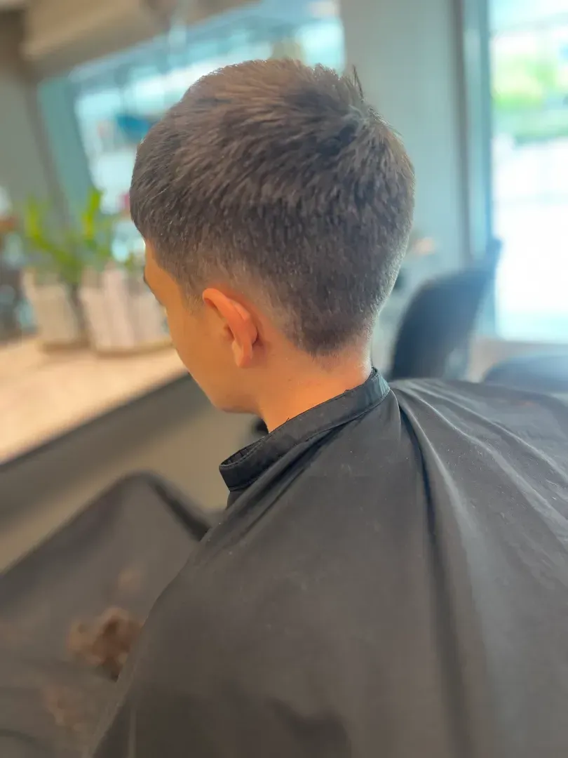 Person with a short, faded haircut at a salon, wearing a black cape.