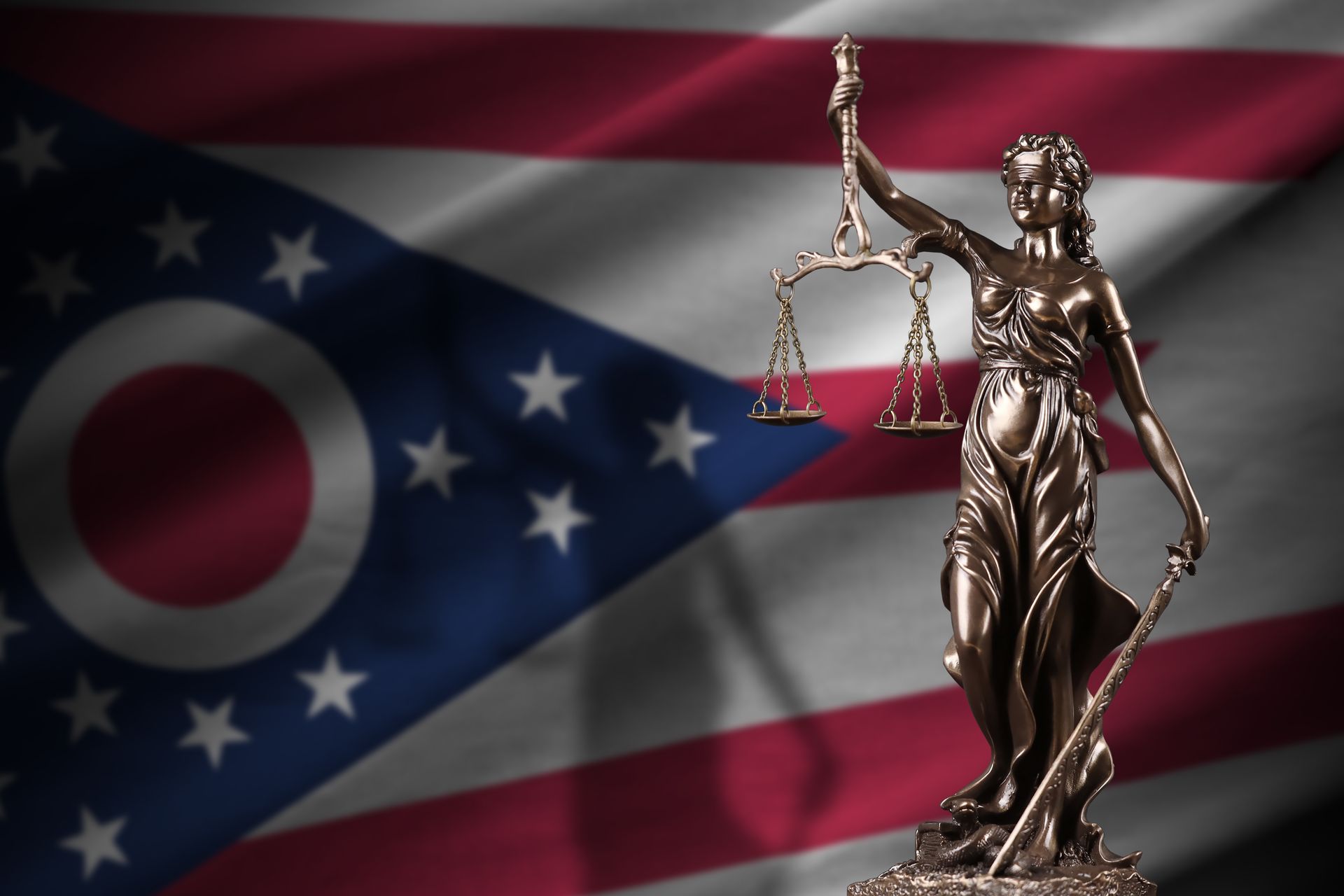 A statue of lady justice stands in front of an ohio flag