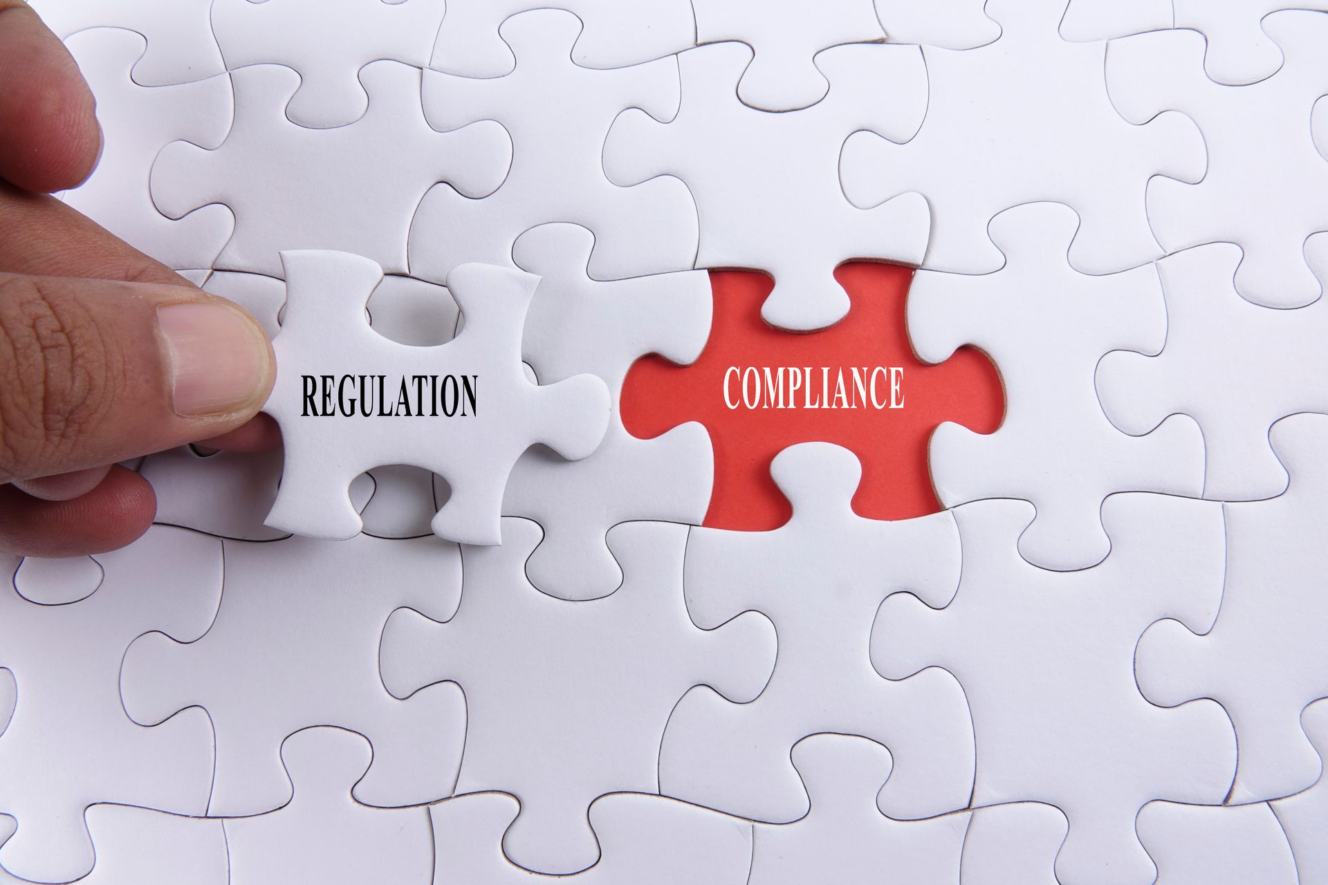 A person is holding a piece of puzzle that says regulation and compliance