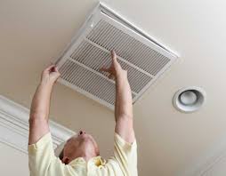 A man is looking up at a vent on the ceiling.