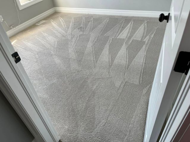 Empty carpeted room with gray walls and white trim, viewed through an open doorway