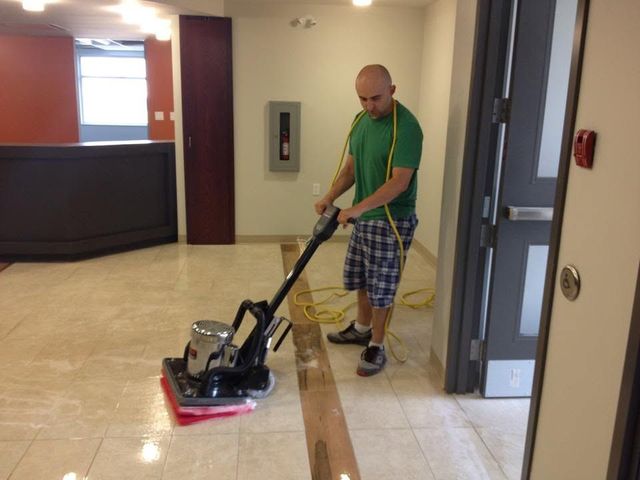 Man using a floor buffer in a hallway with tiled floors and a wooden ramp nearby