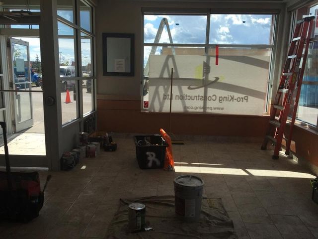 Empty storefront interior with ladders, tools, and a sunlit window under renovation