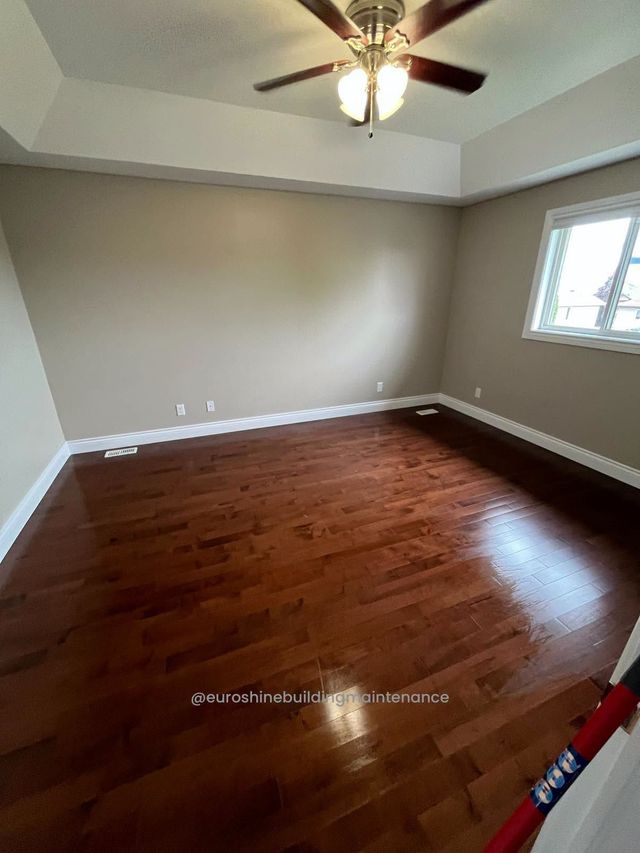 Empty bedroom with polished hardwood floor, gray walls, ceiling fan, and a window letting in daylight