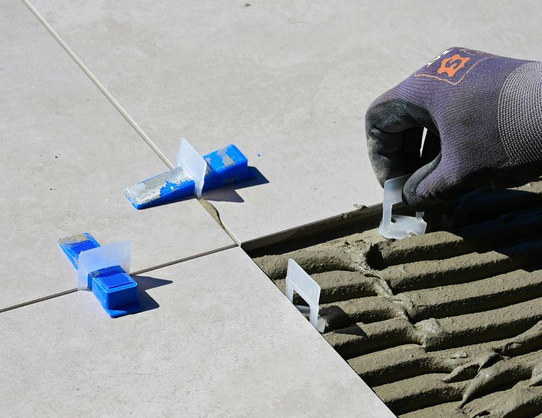 Person installing tile, using leveling clips and grout, outdoors.
