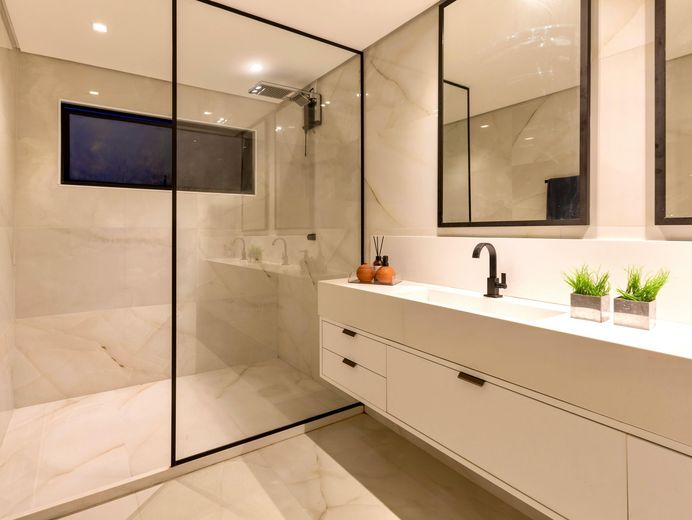 Modern bathroom with marble walls, glass shower, white vanity, and black faucet.
