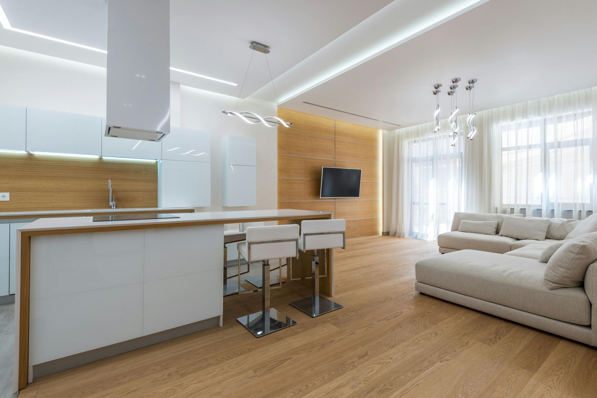 Modern open-plan kitchen and living room with white cabinets, wooden floors, and a light-colored sofa.