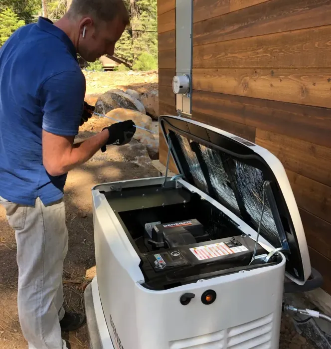 Man working on a white generator outside a building with brown siding. The generator's lid is open.