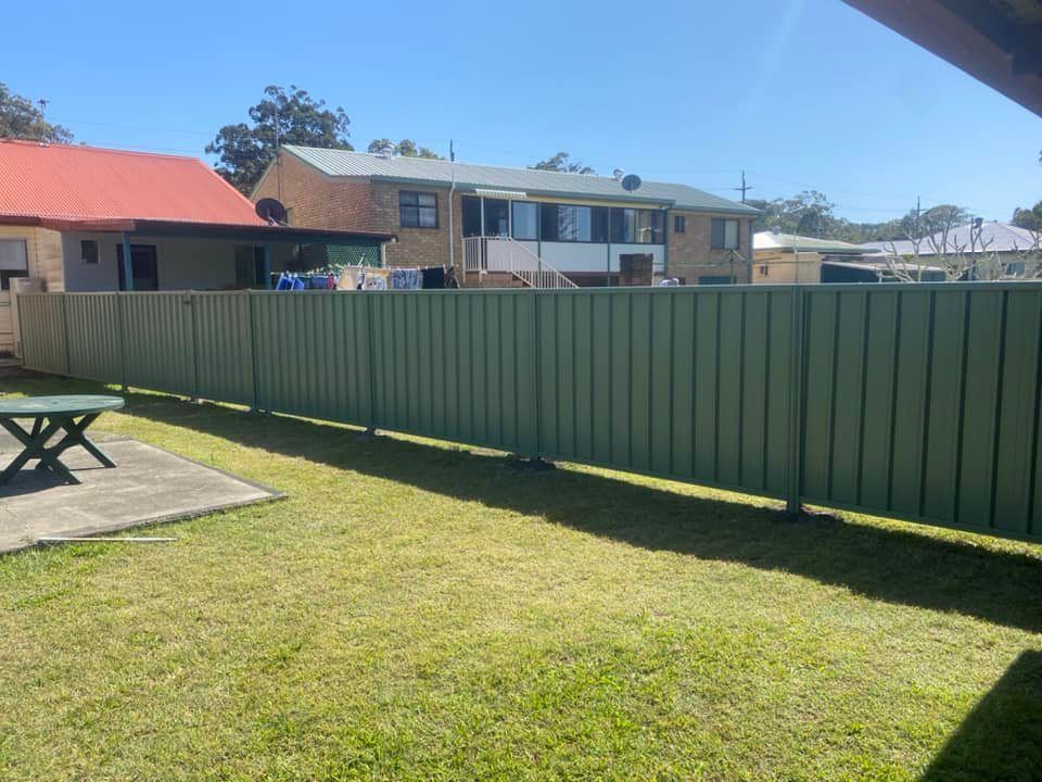 A Green Fence Surrounds A Grassy Yard In Front Of A House — Arecta Fence In Lakewood, NSW