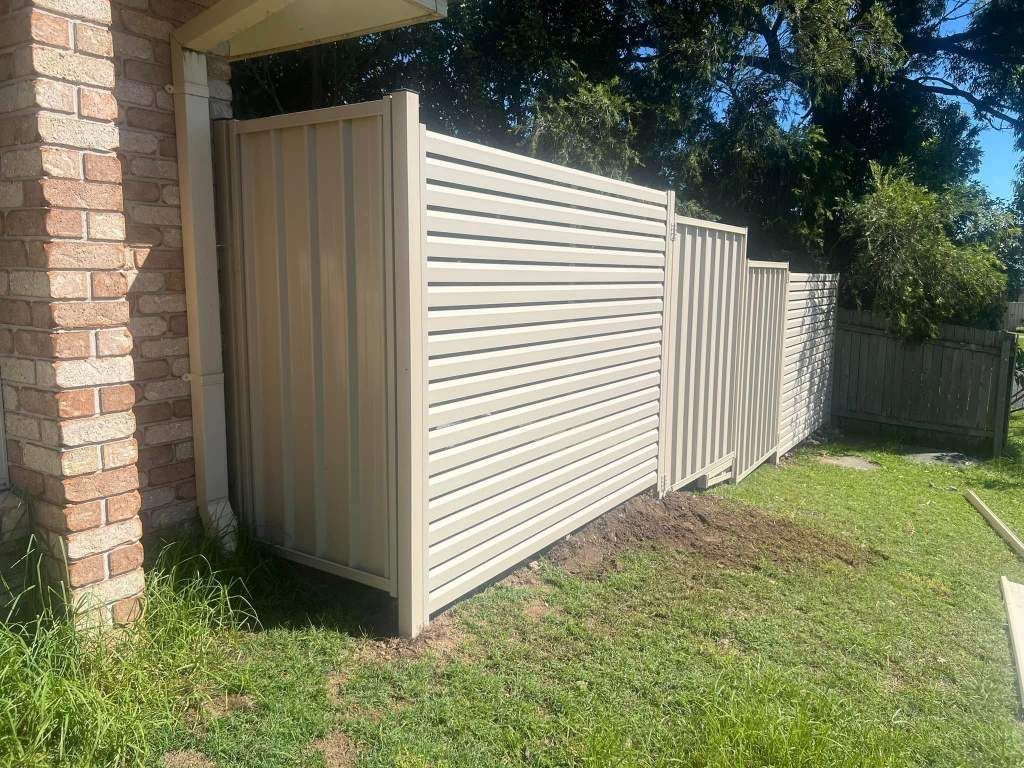A White Fence Is Sitting In The Grass Next To A Brick Building — Arecta Fence In Lakewood, NSW