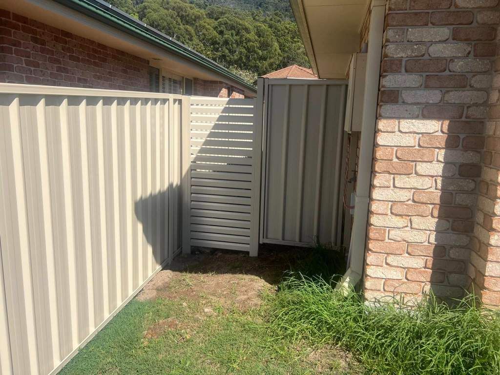 A White Fence Is Next To A Brick Building — Arecta Fence In Lakewood, NSW