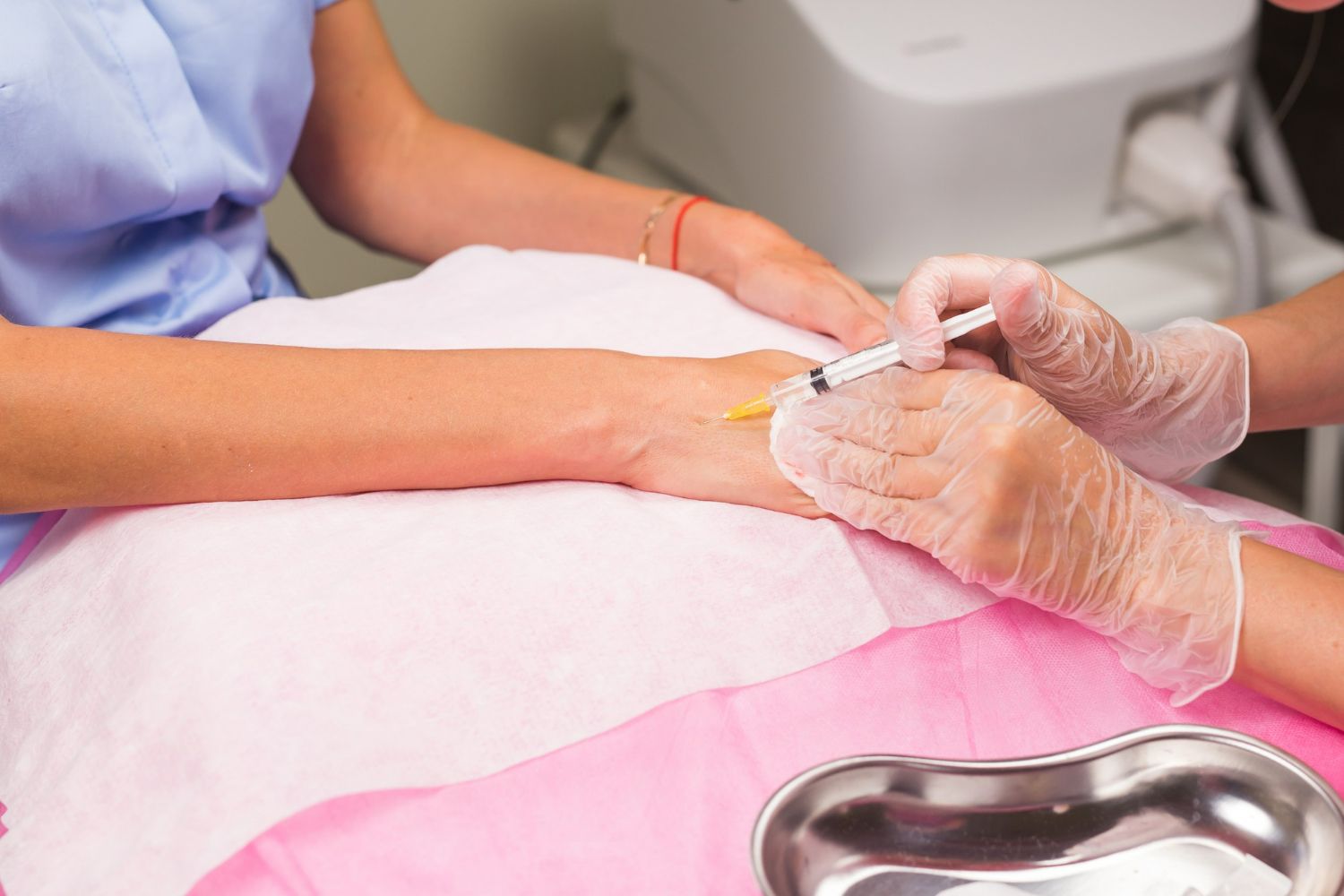 Nurse injecting a needle into a patient's wrist; medical procedure in a clinic.