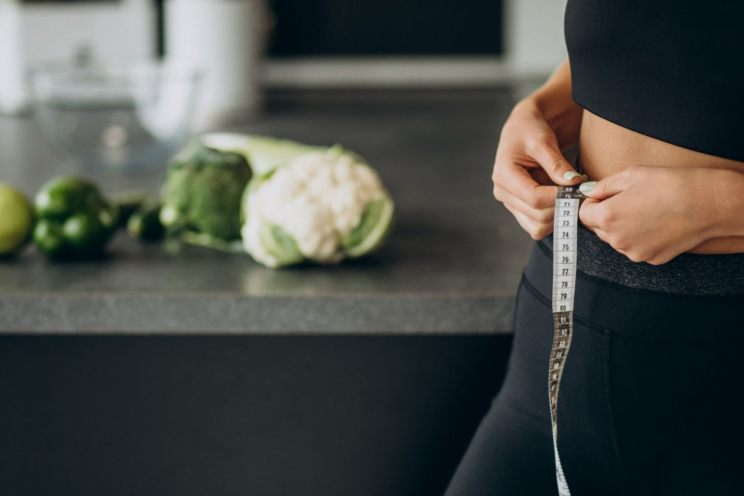 Woman measuring waist with tape; healthy food on counter.