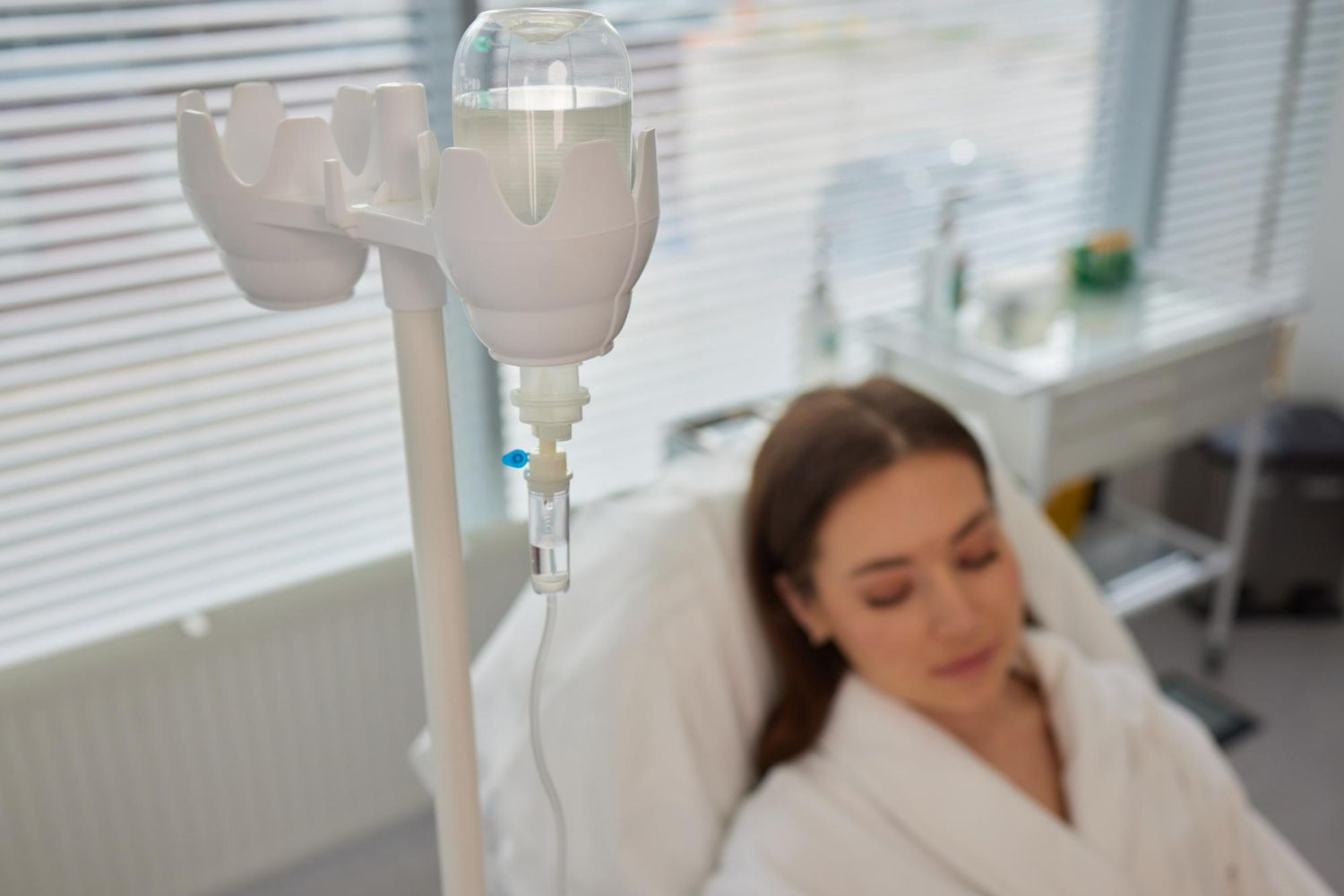 IV drip bag hanging above a person in a white robe, receiving fluids in a medical setting.