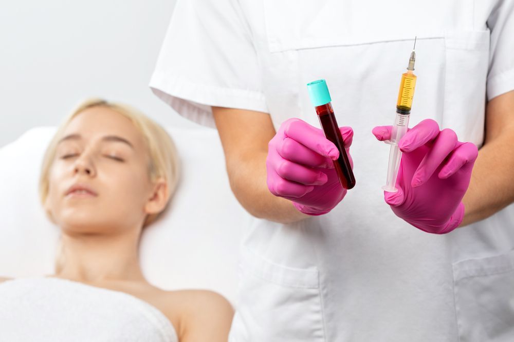 Nurse holding a blood sample and a syringe of yellow liquid, with a patient in a medical setting.