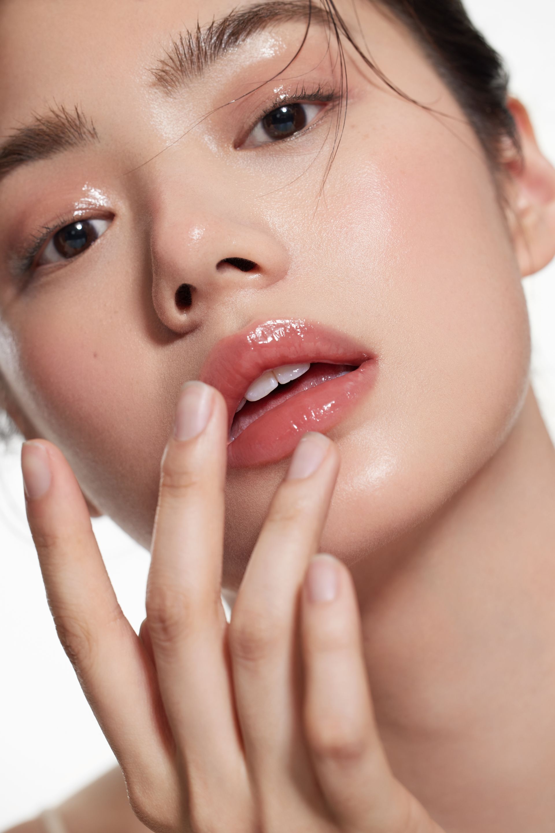 Woman with glossy skin and lips, touching her lips with a finger.