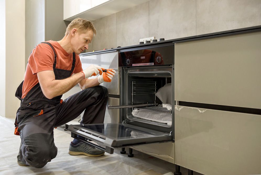 A Man is Fixing an Oven in a Kitchen — Patrick Lunney Home Appliance Service & Repairs in Maudsland, QLD