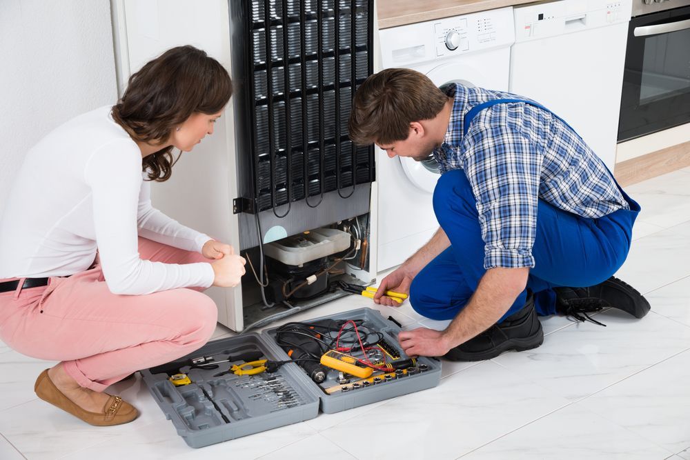 A Man and a Woman Are Working on a Refrigerator in a Kitchen — Patrick Lunney Home Appliance Service & Repairs in Maudsland, QLD
