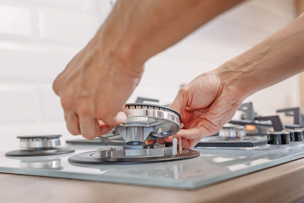 A Person is Fixing a Gas Stove in a Kitchen — Patrick Lunney Home Appliance Service & Repairs in Maudsland, QLD