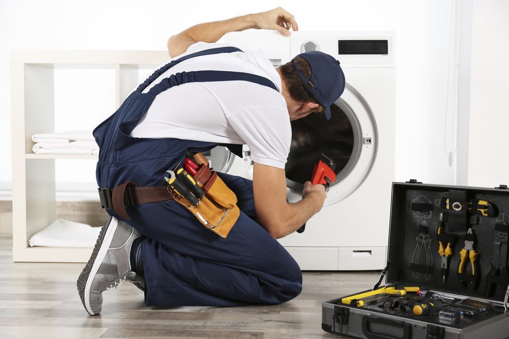 A Man is Kneeling Down Fixing a Washing Machine — Patrick Lunney Home Appliance Service & Repairs in Maudsland, QLD