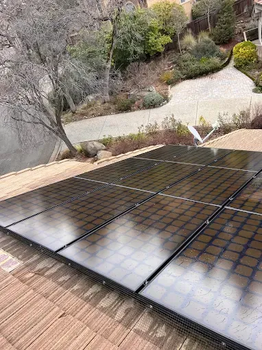 Solar panels on a terracotta roof with a paved driveway and hillside in the background.