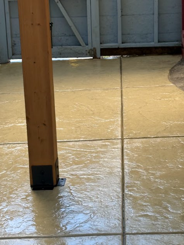 Wet, golden-colored concrete patio with visible grout lines and a wooden support column with a black base.