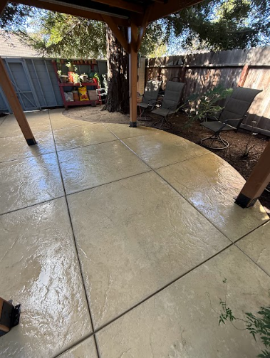 Outdoor patio with tan concrete flooring, wooden posts, and seating.