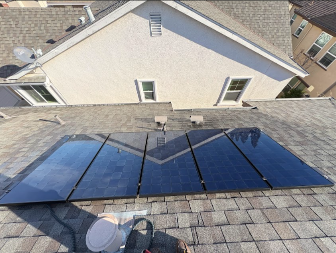 Solar panels installed on a residential roof, angled toward the viewer. Panels are black, set against gray shingles.