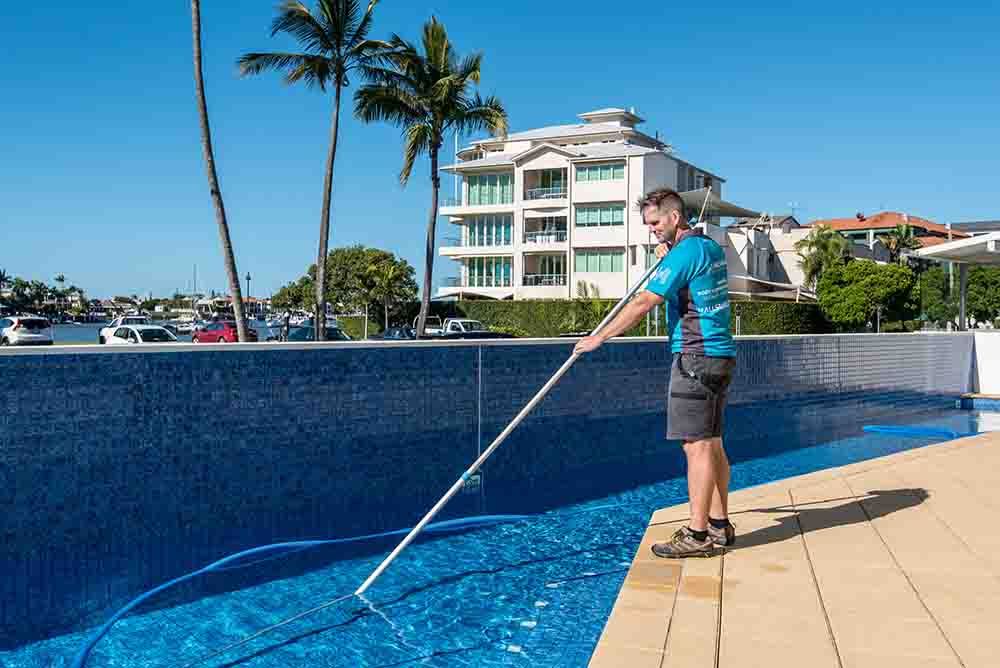 Man Cleaning the Swimming Pool With Long Brush — Hallsmark Property Services