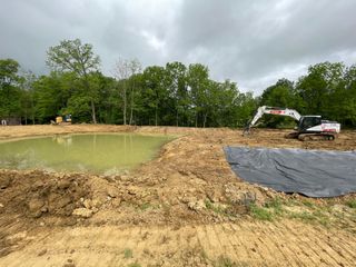 An excavator is digging a pond in the middle of a dirt field.