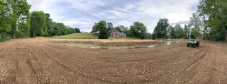 A tractor is plowing a field with a barn in the background.