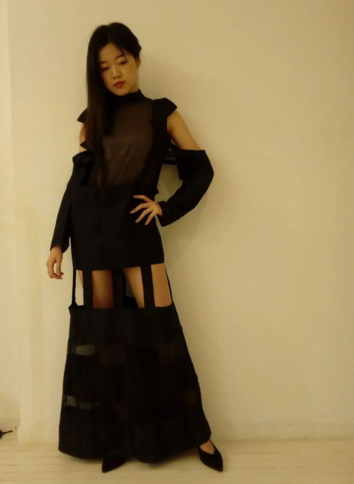 Una donna in abito nero è in piedi davanti a un muro bianco