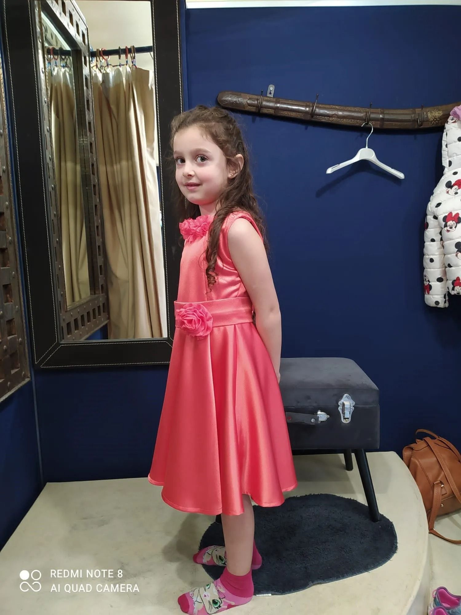 Una bambina con un vestito rosa è in piedi in uno spogliatoio.