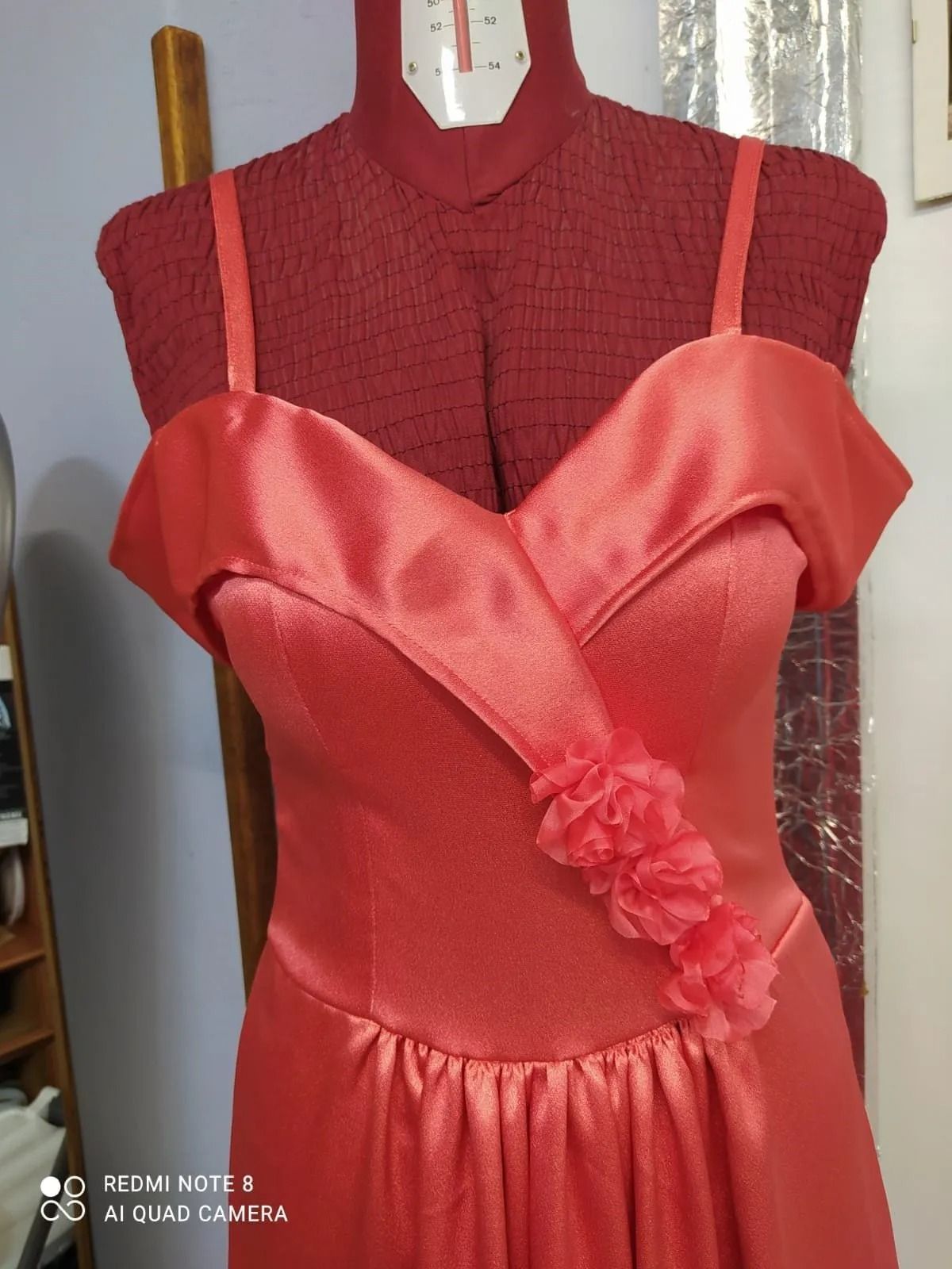 Un vestito rosso con un fiore sul lato è su un manichino.