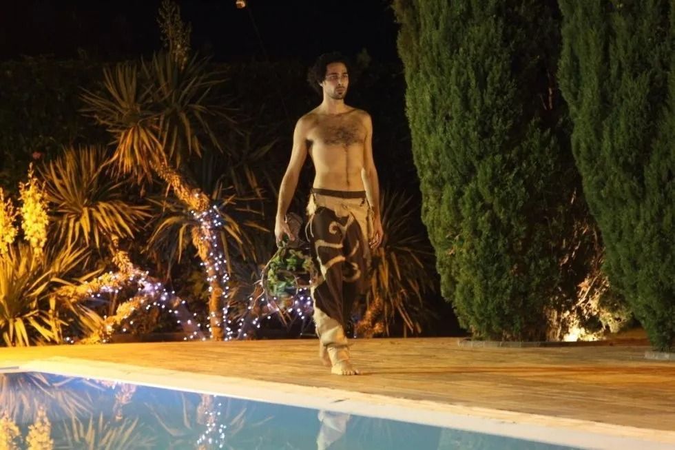 Un uomo a torso nudo è in piedi accanto a una piscina di notte.