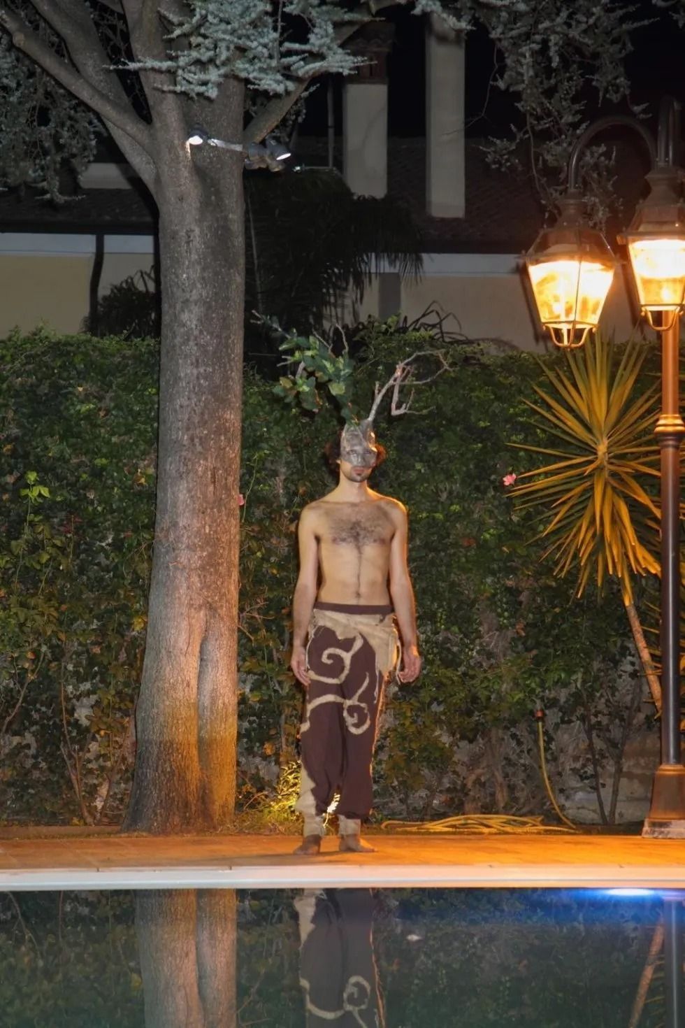 Un uomo a torso nudo è in piedi accanto a una piscina di notte.