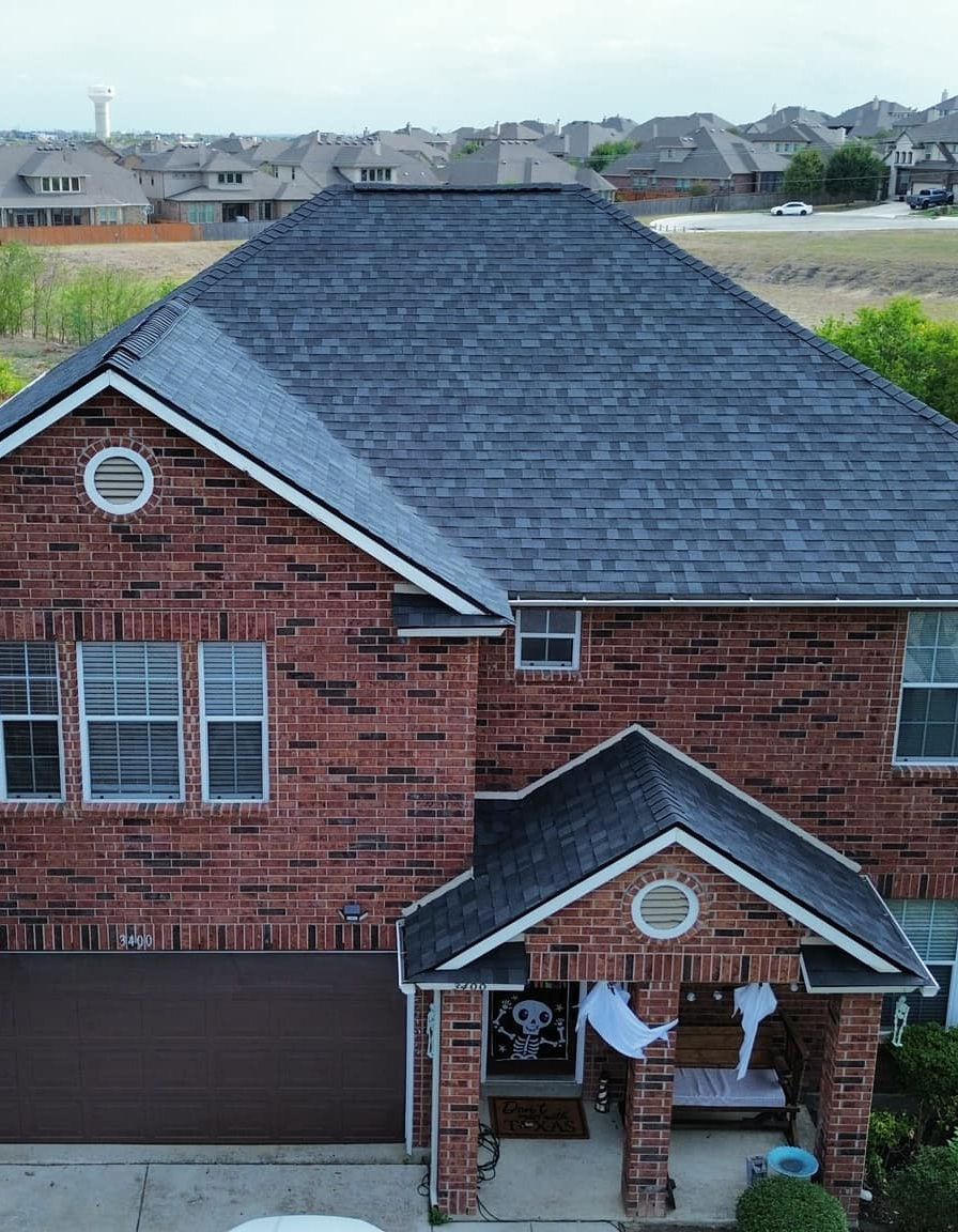 An aerial view of a brick house with a black roof.