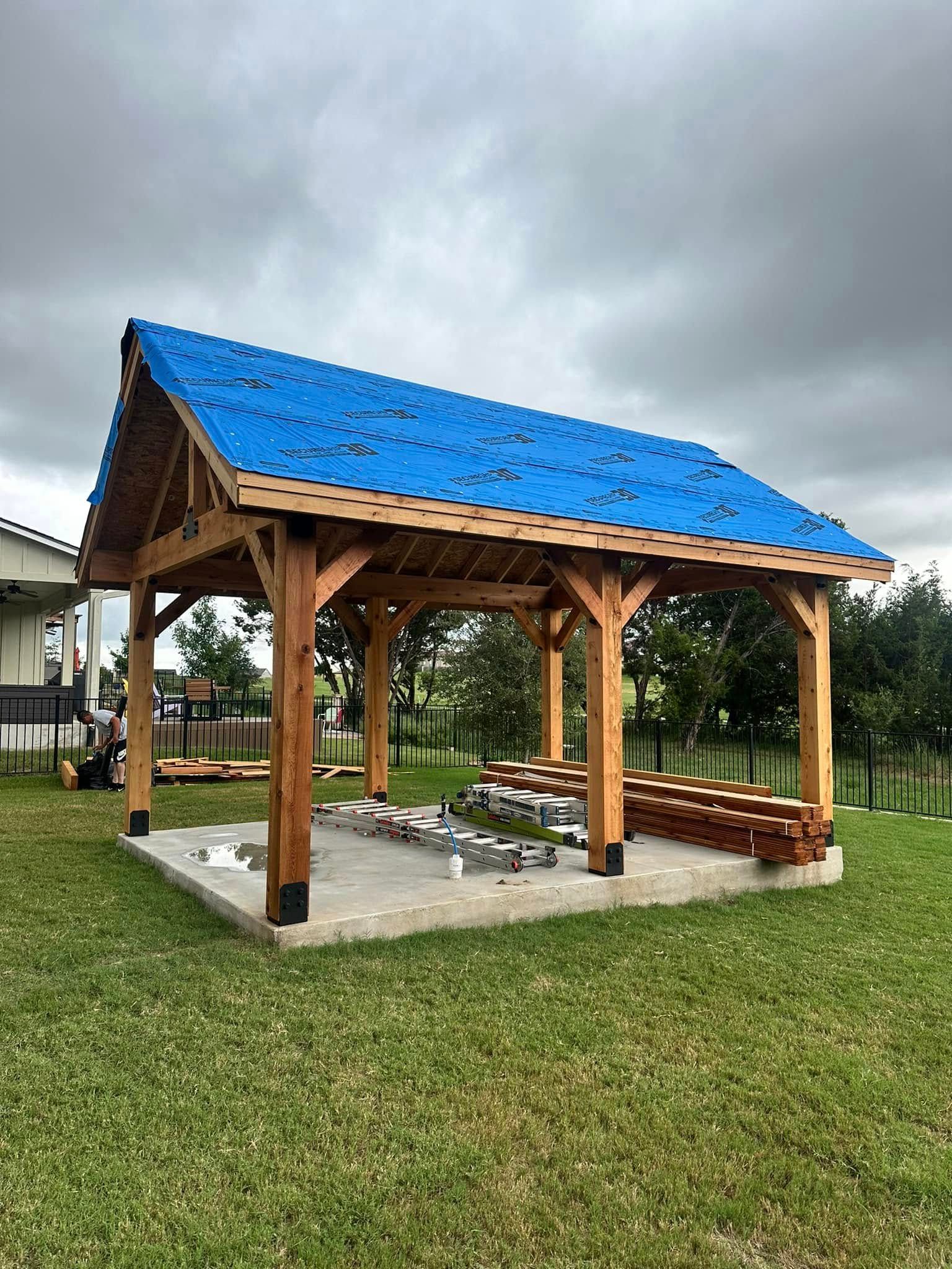 A wooden pavilion with a blue roof is sitting in the middle of a grassy field.