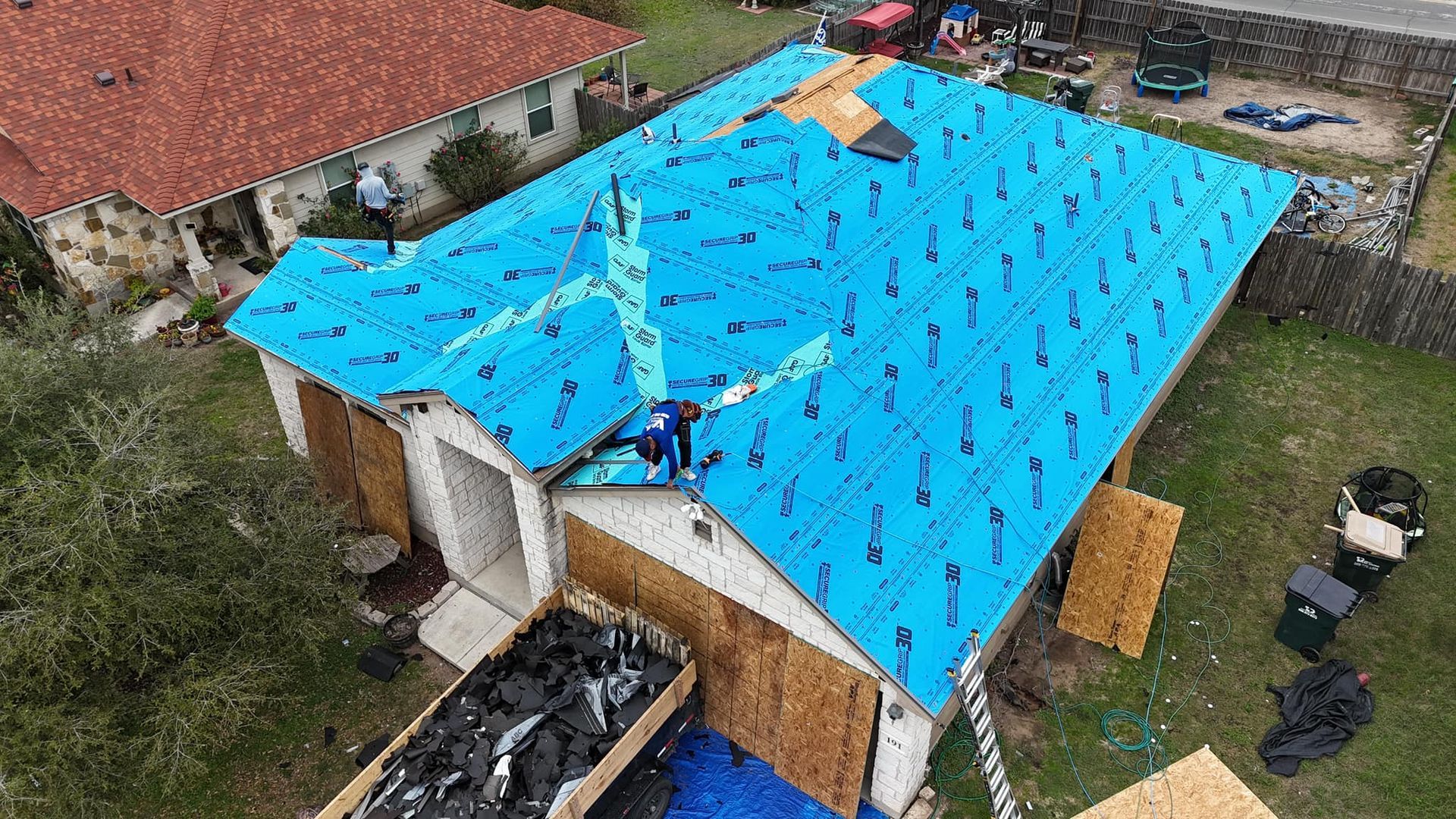An aerial view of a house with a blue roof being installed.