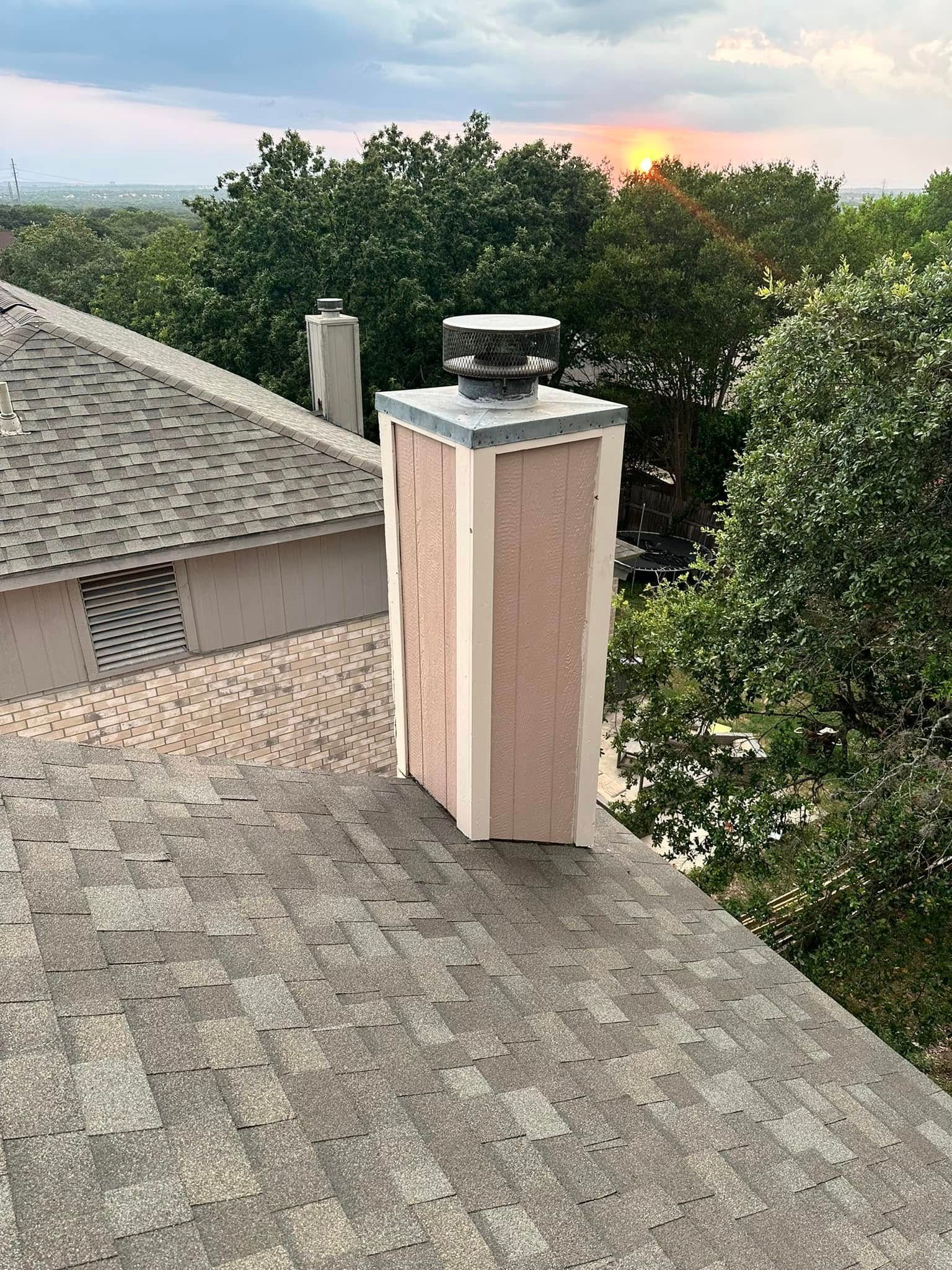 A chimney is sitting on top of a roof with trees in the background.