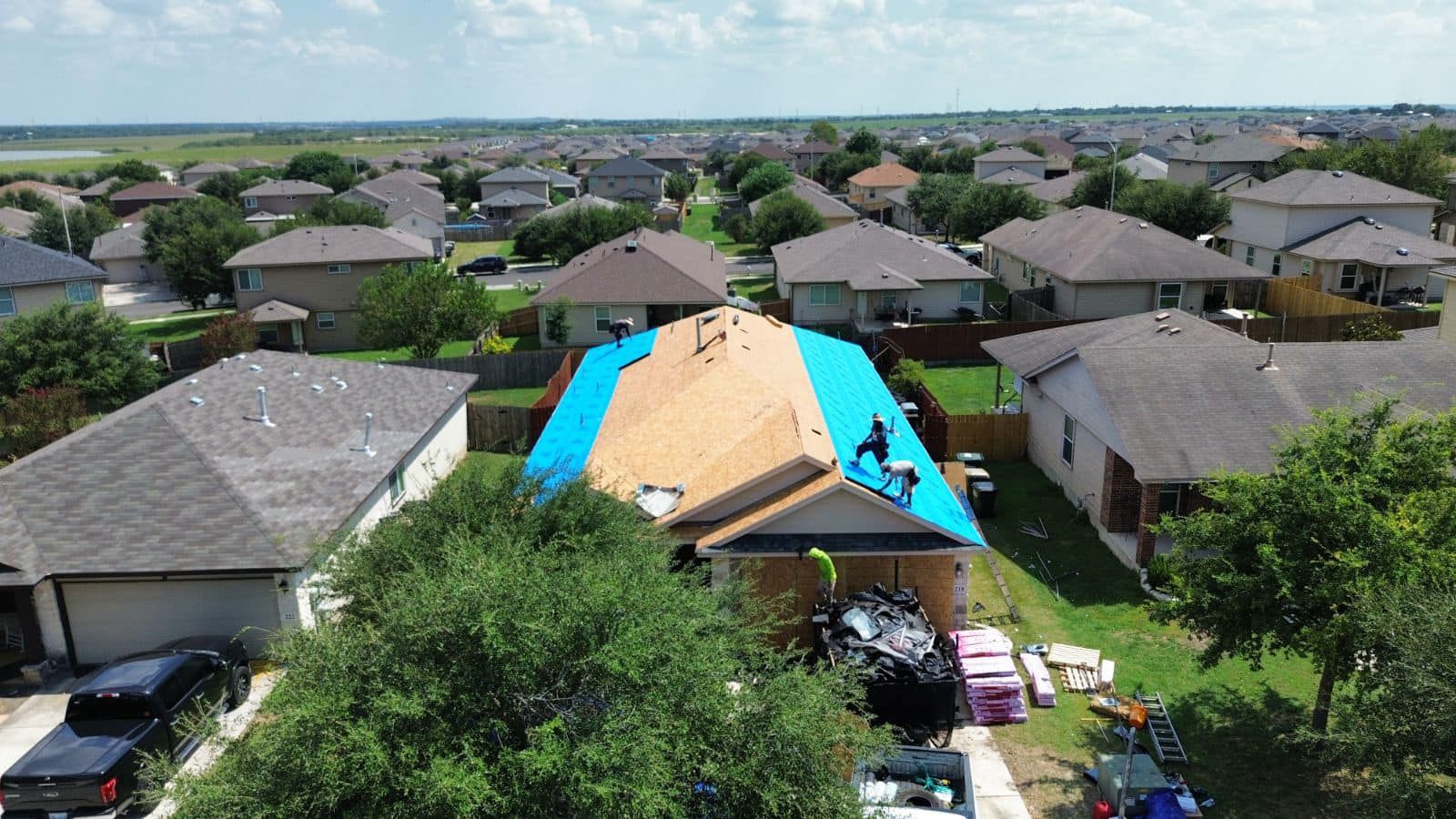 An aerial view of a house being roofed in a residential area.