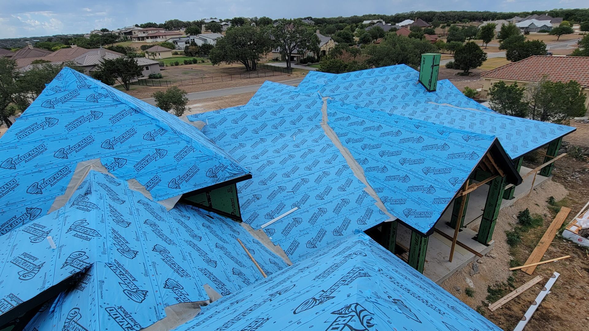 An aerial view of a house under construction with a blue tarp on the roof.