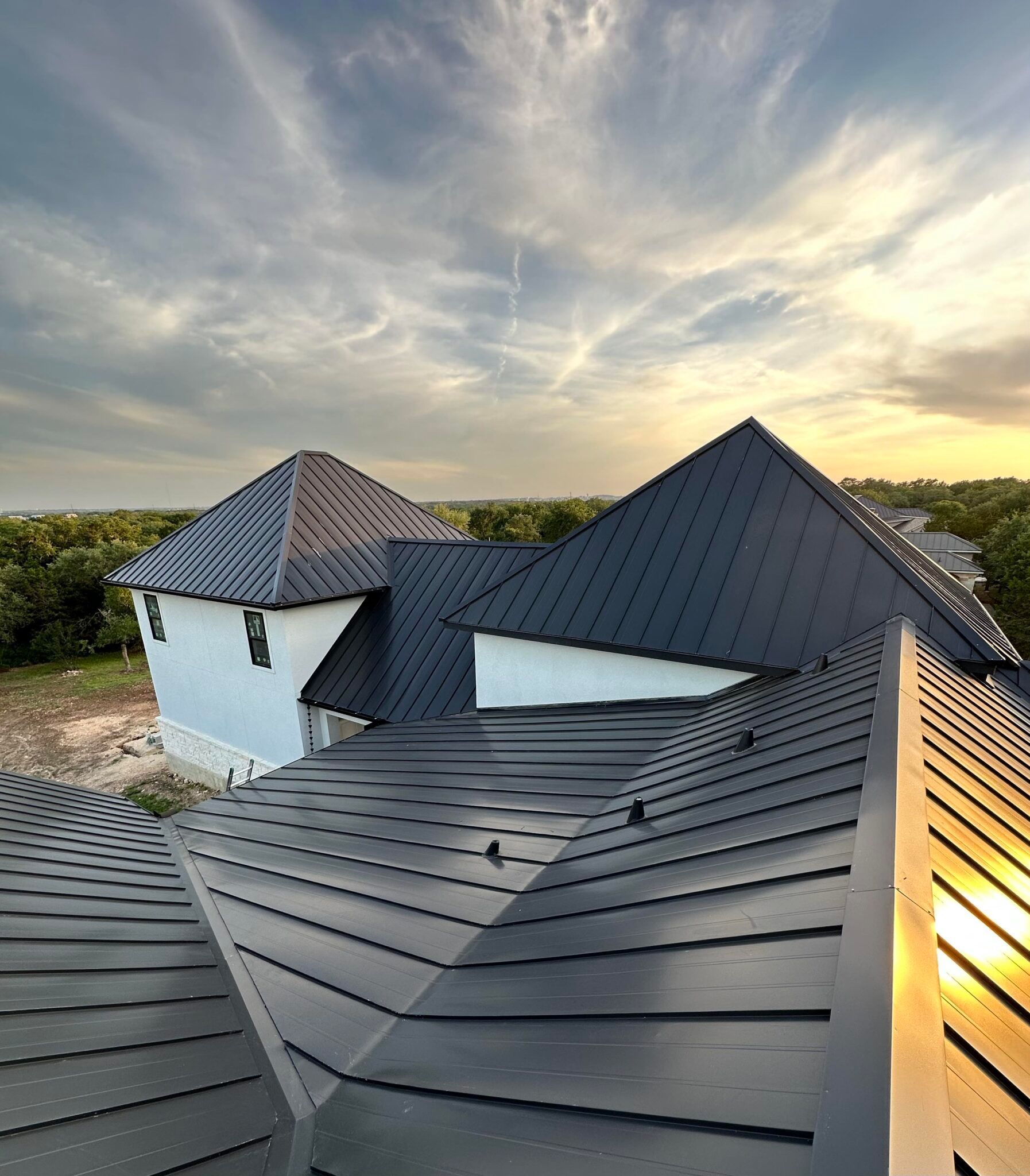 An aerial view of a house with a black roof and a sunset in the background.