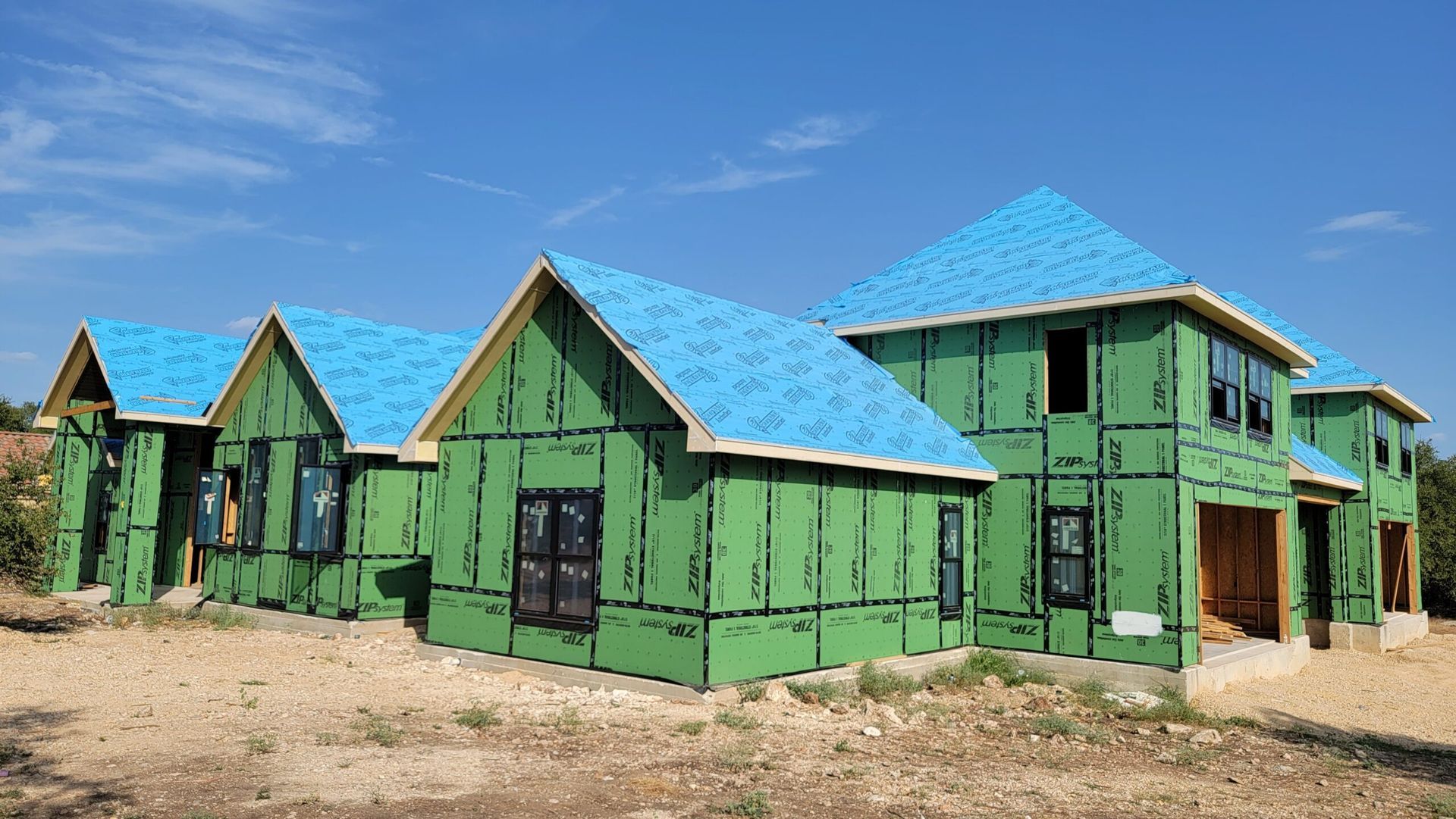A row of green houses with blue roofs are being built.