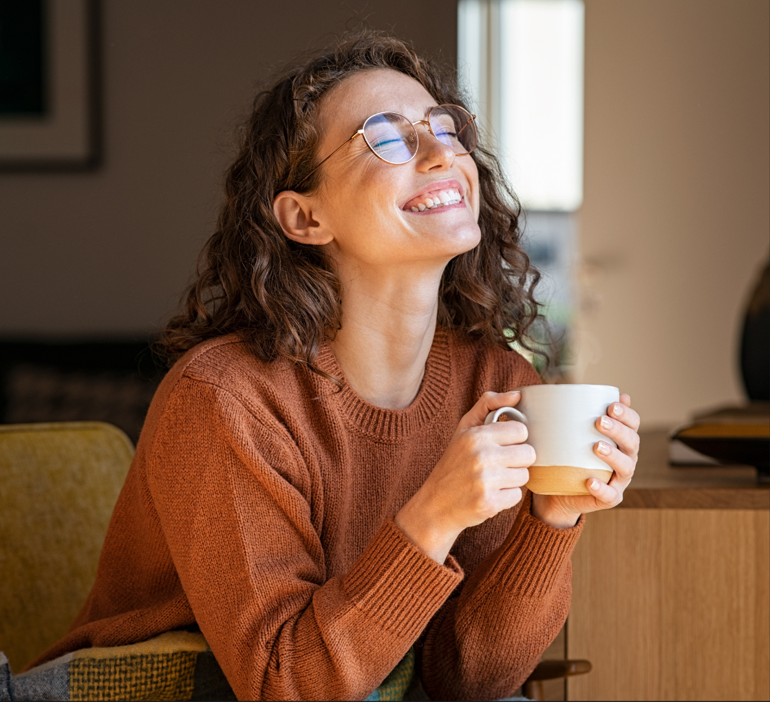 A woman is smiling while holding a cup of coffee.